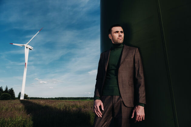 企业家一个穿着西装 穿着绿色高尔夫球衣的男人站在风车旁边 背景是田野和蓝天裸体行政便携式