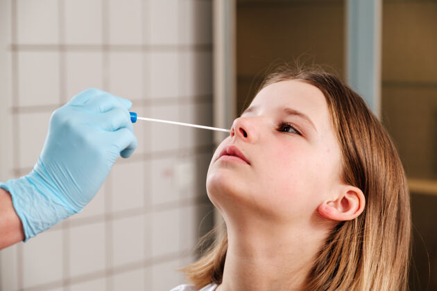 女人医生的手拿着棉签 从一个女孩的鼻子里取出一份分析报告诊所室内分析