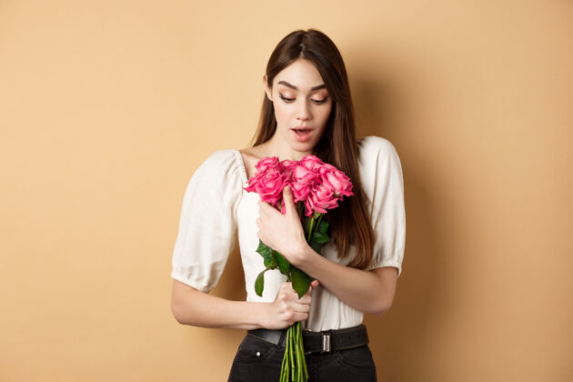 感动情人节惊喜的女孩在约会时收到情人的礼物 看着美丽的花束 捧着米色背景的玫瑰礼物神奇嘴唇
