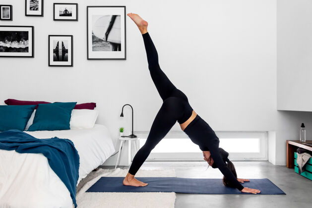 普拉提一个女人在现代简约卧室练习瑜伽时 一条腿朝下对着狗劈腿女人瑜伽健身