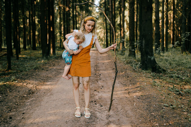 木头年轻的母亲拿着棍子在森林里抱着她的儿子森林抱着衣服
