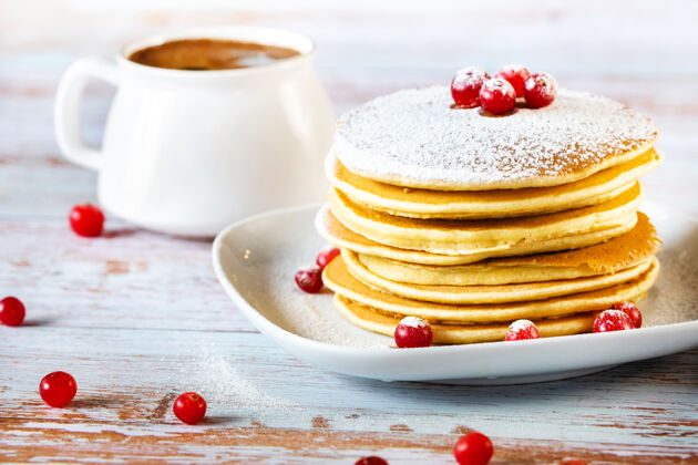 堆栈早上的早餐是在木桌上放着小红莓和糖粉的薄煎饼和一杯咖啡蛋糕光明热蛋糕