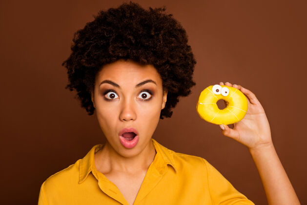 不健康这个蛋糕可以说惊艳的深色皮肤的特写照片女士拿着五颜六色的甜甜圈焦糖眼睛人脸画着穿黄色衬衫孤立的棕色女性甜点无言