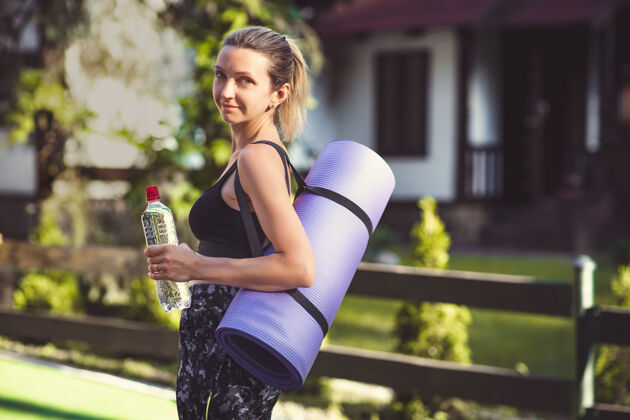 成人一个穿着运动服的女人 运动后拿着瑜伽垫和水瓶健康女性运动