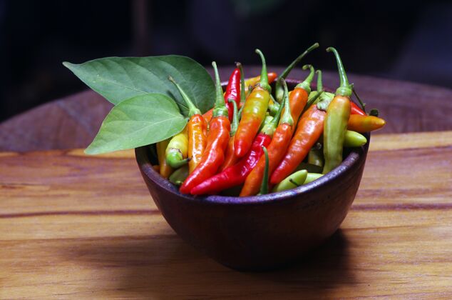 辣新鲜的生红辣椒放在一个有绿叶的粘土盘子里碗胡椒辣椒