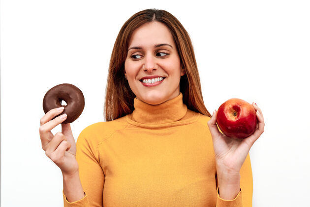 光一只手拿着甜甜圈 另一只手拿着苹果 一个面目全非的女人在怀疑吃什么饮食护理苹果