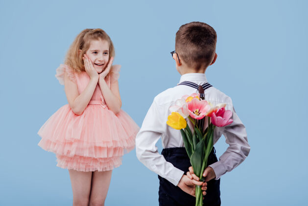 惊人两个小孩 一个男孩拿着花 一个女孩穿着粉红色的裙子 孤零零地站在蓝色的墙上花小愉快