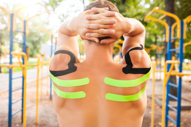 治疗不可辨认的年轻白种人专业健美运动员 赤裸的肌肉肩膀上贴着黑色和绿色的运动生理录像带 在运动场上摆姿势损伤身体肌肉