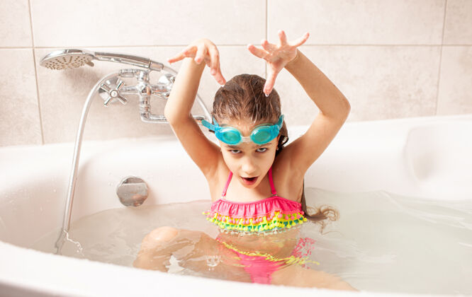 洗脸有趣的小女孩在泳衣和泳镜描绘了一个海怪在家洗澡水疗幸福可爱