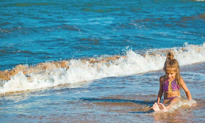 日落小积极的女孩坐在海边 享受在一个阳光明媚的夏日在假期海浪贝壳欢乐活动