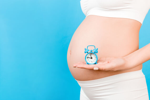 产妇穿着白色内衣拿着闹钟的孕妇未出生肚子内衣
