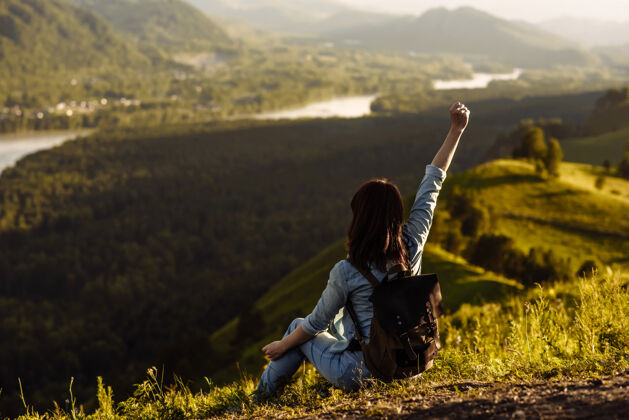 远足者坐在山上的年轻快乐的女旅行者向上举手女孩年轻人小山