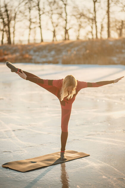 湖冬天 一个女孩在日落时在湖边的冰上做瑜伽运动姿势霜冻