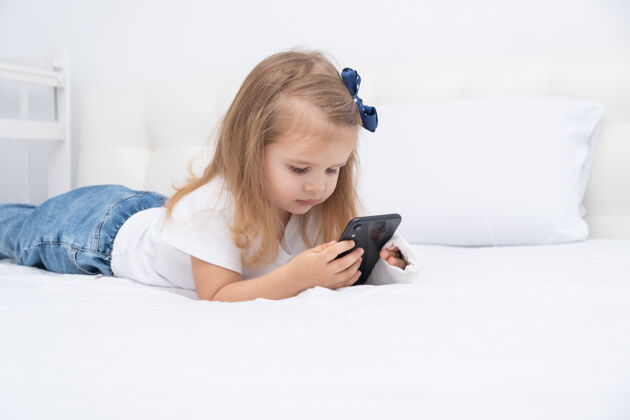 矫形手拿石膏的小女孩躺在床上用智能手机 看动画片或教育视频健康童年事故