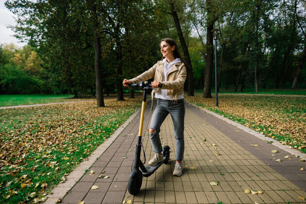 生态年轻漂亮时尚的女子骑着电动踏板车经过秋园 生态交通积极车辆秋天