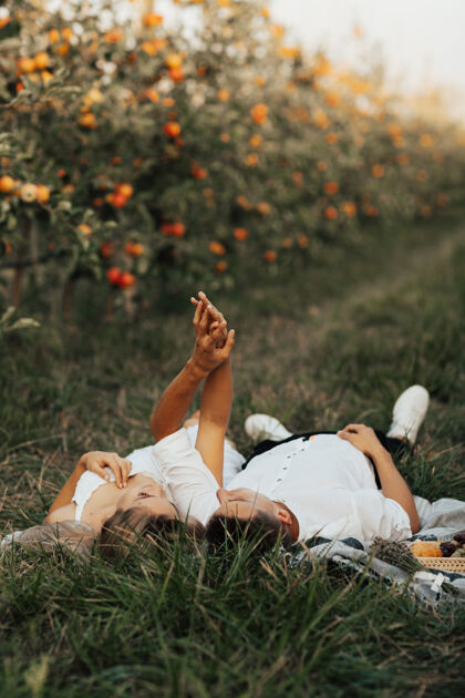 年轻一对美丽的笑脸情侣在苹果园享受野餐果园他们手牵着手躺着乡村欢呼农业