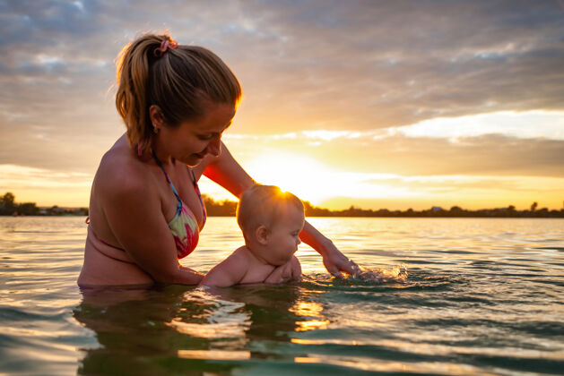 水快乐的白种人的母亲教游泳小可爱的微笑的婴儿在海水中的侧视图快乐自然海洋