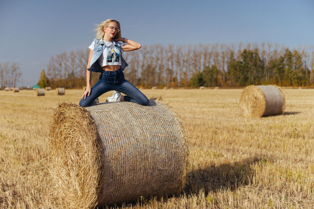 干草一位年轻漂亮的女村民 穿着牛仔裤 站在地里的一捆干草上姿势草包村庄