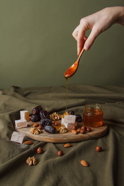 吃准备喝茶手拿勺子滴蜂蜜各种各样的甜食 坚果和蜂蜜放在木制的砧板上健康的甜食 美味的甜点 天然甜食美味杏仁食物