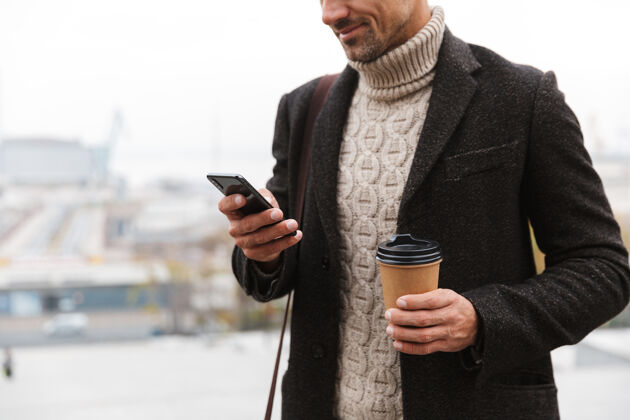 电话一张30多岁的欧洲男人的肖像 穿着夹克 拿着手机 端着外卖咖啡 走在城市街道上手机漫步时尚