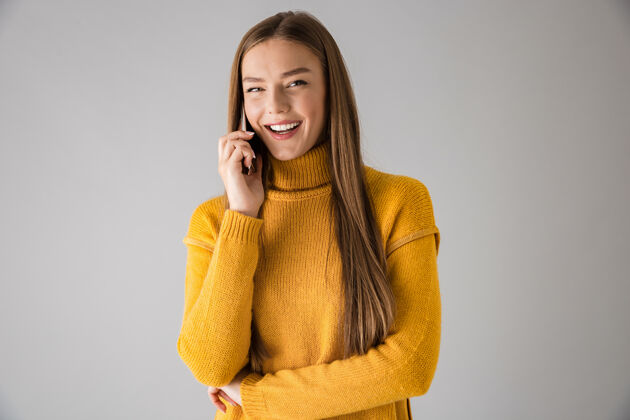 站立一个美丽快乐的年轻女子隔着灰墙用手机交谈的画面白种人休闲毛衣