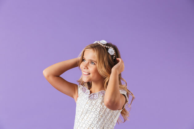 服装画中 一个微笑的 快乐的 穿着公主裙的漂亮女孩孤立地站在紫罗兰色的墙上 望着别处优雅表演孩子