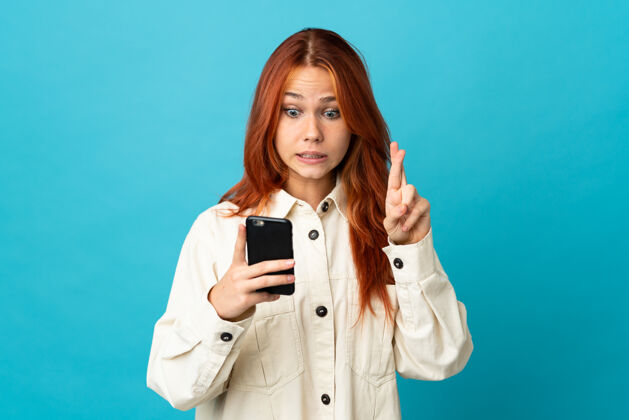 电话一个俄罗斯女人在蓝色的世界里用手机和手指交叉手势幸运红
