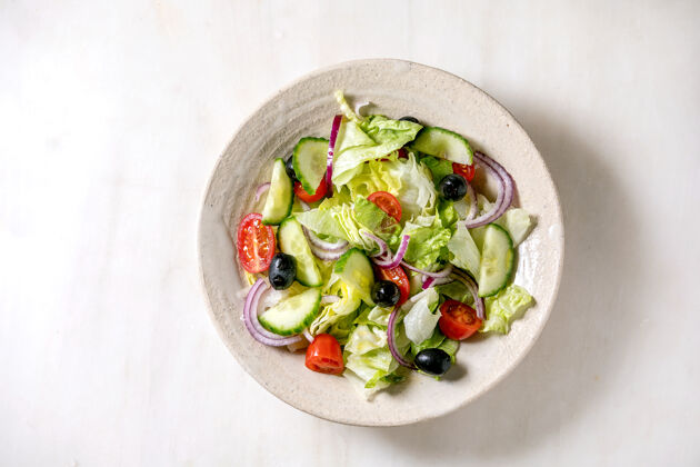 平铺经典的蔬菜沙拉 西红柿 黄瓜 洋葱 色拉叶和黑橄榄在白色陶瓷盘子里白色大理石背景平铺 复制空间绿色午餐洋葱