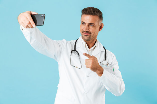 表情这张照片是一位身穿白大褂 手持听诊器 孤零零地站在蓝色墙壁上的医生自拍的照片从业者中年外套