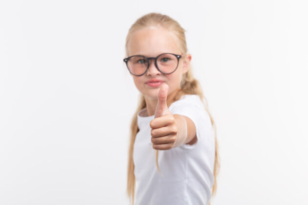 视力漂亮的小女孩戴着眼镜 竖起大拇指站在白色的地板上童年视力测试眼镜