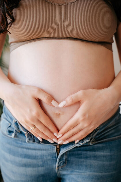 家庭一个怀孕的女人把她的手放在她的肚子上 以心脏的形式在怀孕6个月的时候等孩子父母年轻产妇
