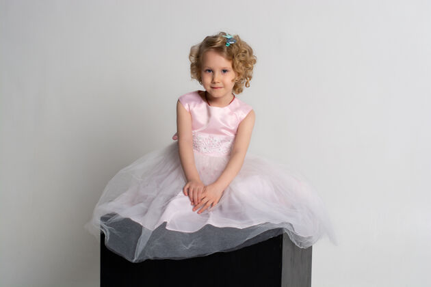 健康一个小女孩穿着粉红色的裙子 头戴皇冠 坐在白色背景的黑色立方体上童年服装人类