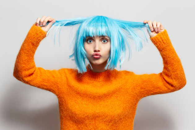 吻麻布女孩的肖像 抱着蓝色的头发 穿着白色背景下的橙色毛衣成人尼斯年轻