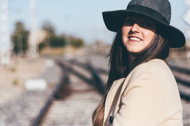 微笑在废弃的铁轨上穿着米色雨衣戴着帽子的快乐女人货车时间火车头