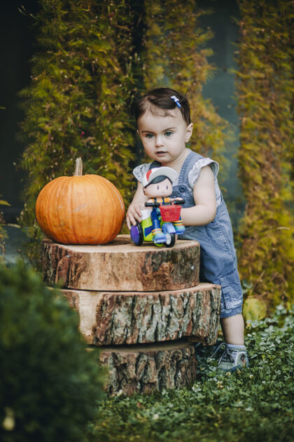 婴儿可爱的宝宝在自家院子里玩着她的玩具 旁边装饰着大南瓜树桩装饰可爱食物