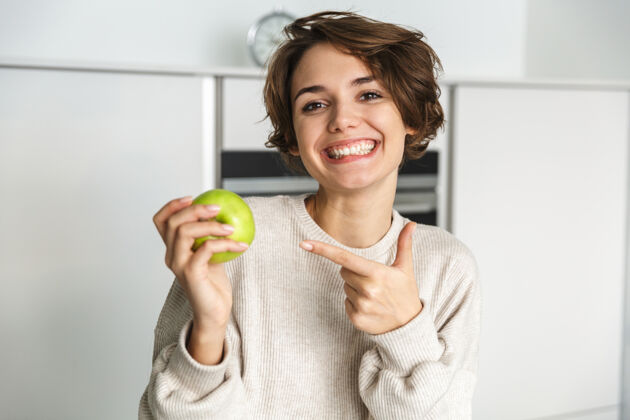 苹果微笑的年轻女子在厨房里拿着青苹果新鲜好吸引力