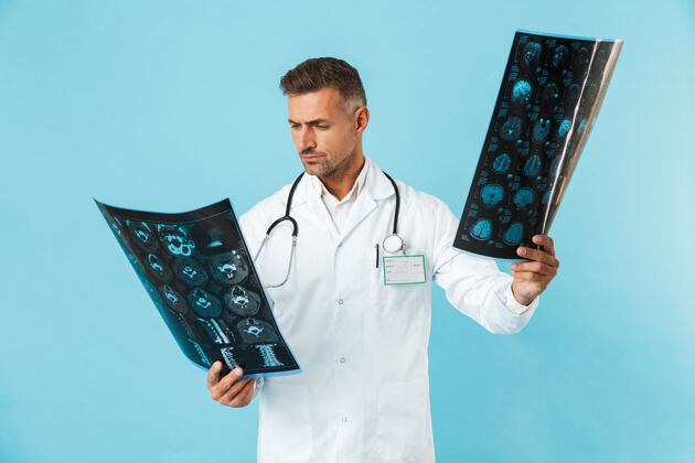 成人30多岁的医护人员手持听诊器 手持x光片 孤零零地站在蓝色的墙上诊所X光医疗