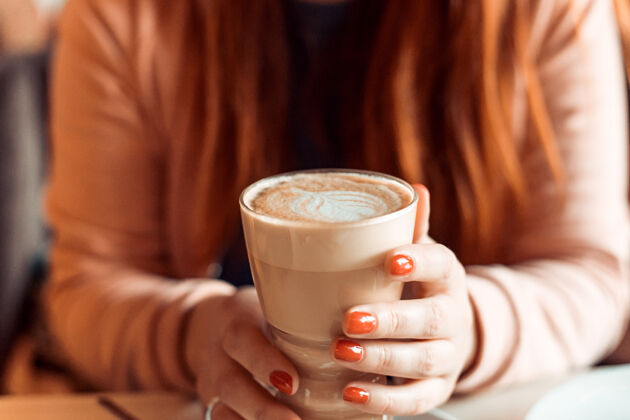 拿铁红指甲的女人坐着 手里拿着一杯热咖啡咖啡特写手拿拿铁 红指甲自助餐厅浪漫杯子