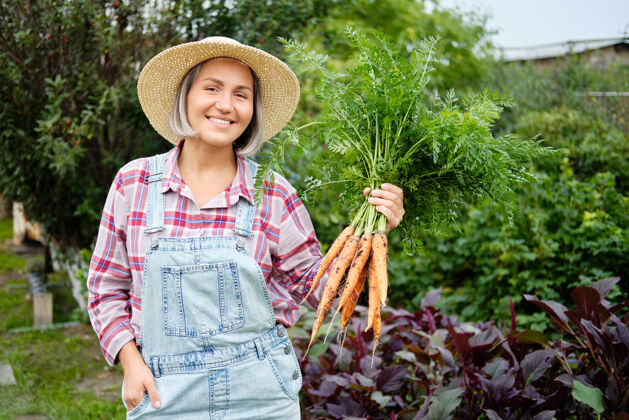 营养戴着帽子的可爱女孩在花园里摘胡萝卜花园.秋天蔬菜丰收蔬菜生态农产品