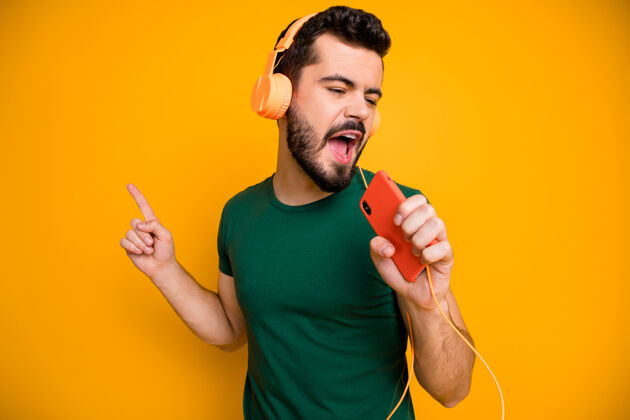 歌手积极开朗的家伙听立体声音乐从橙色耳机使用手机作为麦克风音乐T恤想象