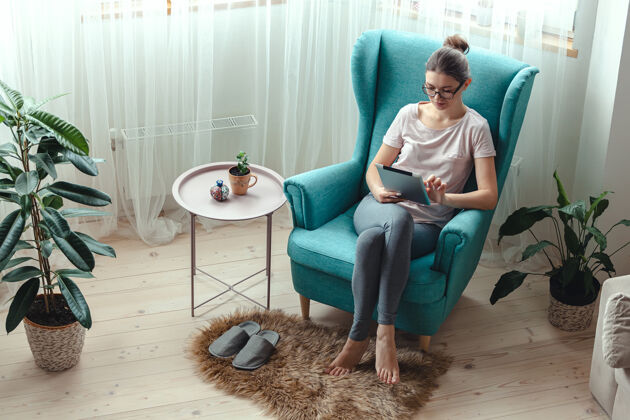 互联网坐在舒适的椅子上使用平板电脑的年轻女士眼镜沟通数字平板电脑