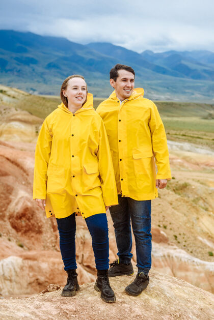 山穿着黄色夹克的年轻快乐的游客在阿尔泰的彩色山脉上户外男人快乐