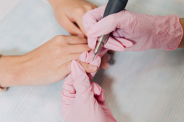手套修指甲的过程一位戴着粉色橡胶手套的用电动指甲打磨指甲文件.female把手收起来电美甲研磨