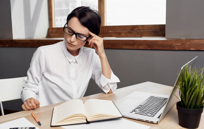 坐着一位女士在办公室里的笔记本电脑后面工作 商务财务和桌上的记事本微笑公司笔记本电脑