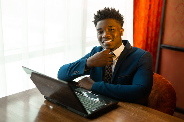 项目帅气的非洲年轻人穿着西装 在室内拿着笔记本电脑商业高管学生