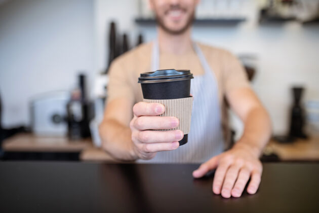 触摸咖啡你纸一杯咖啡 咖啡店的吧台后面站着一位咖啡师 他伸出的手上有盖子正面男士饮料