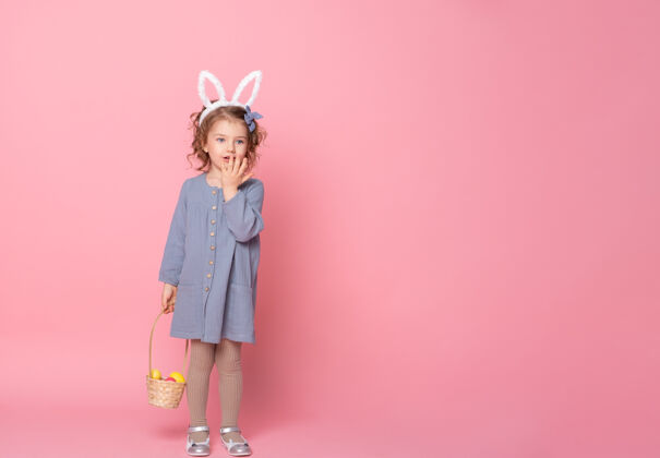 童年有趣的小女孩在复活节兔子耳朵和蓝色连衣裙举行篮子彩色彩蛋粉红色绘画肖像惊喜