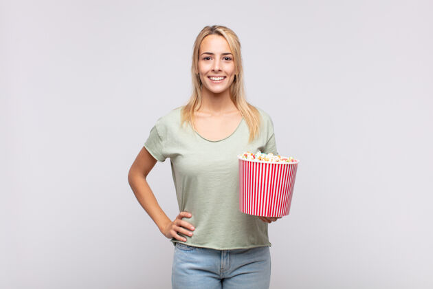 美丽一个拿着爆米花桶的年轻女子 手放在臀部 面带微笑 态度自信 积极 自豪 友好电影院快餐电影