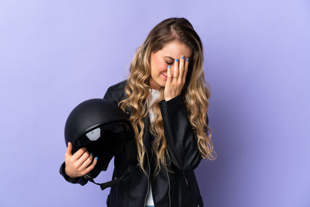 肖像巴西年轻女子手持摩托车头盔孤立在紫色的疲惫和病态的表情司机人金发