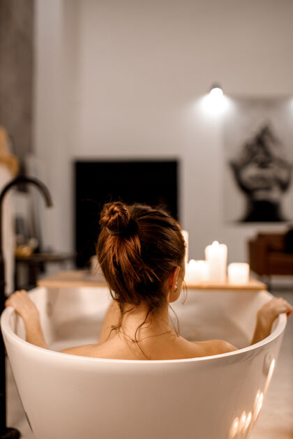 水疗年轻女子放松在美丽的老式浴缸泡沫充分复古浴室装饰蜡烛保健泡沫清洁